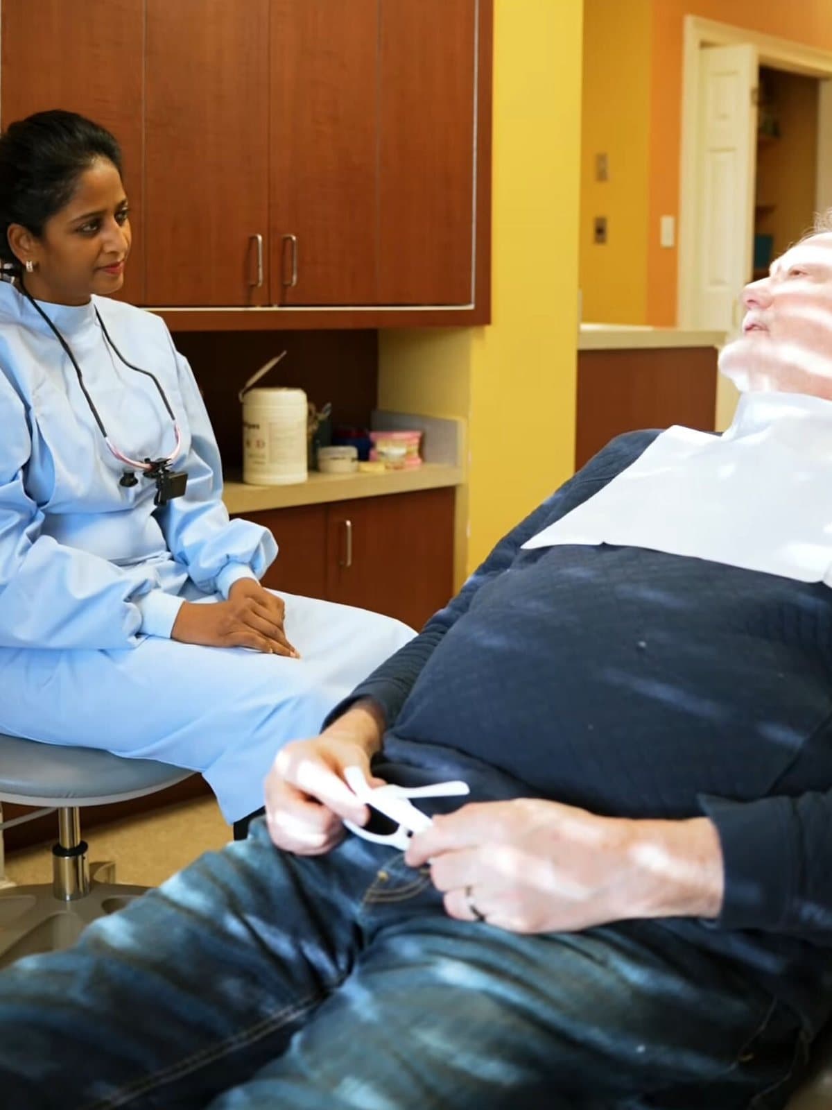 Dr. Madhavi Bhoompalli seated chairside, talking with a patient in the treatment room